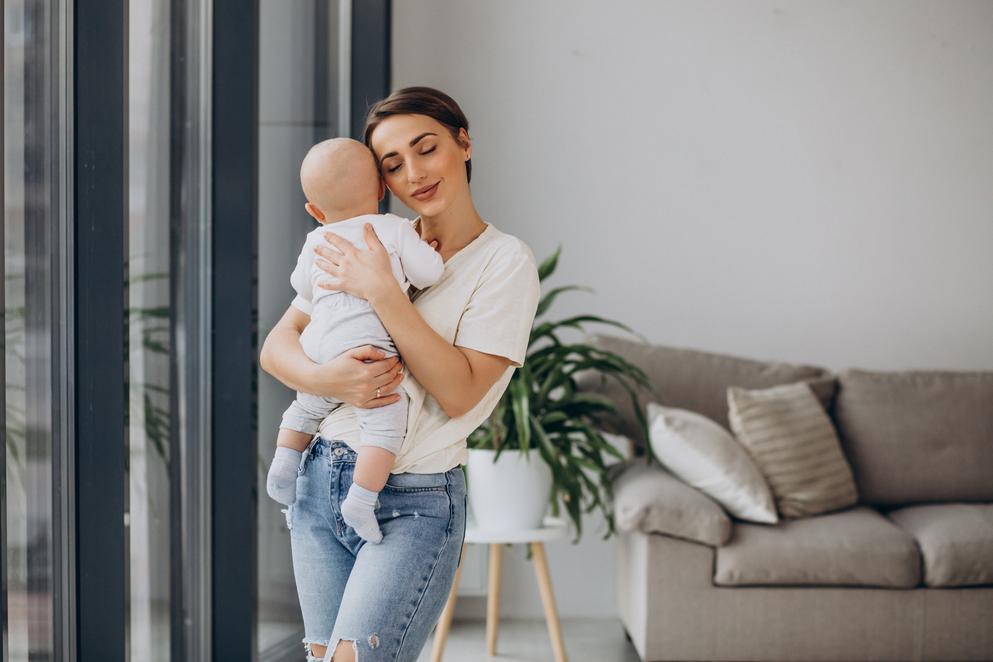 mother with baby son standing by window smiling